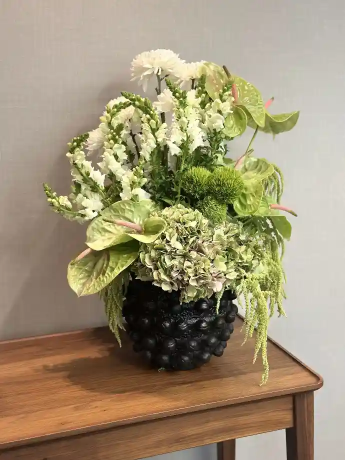 White and green floral arrangement in a black textured vase